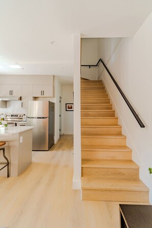 A modern kitchen with stainless steel appliances, a wooden staircase, and a minimalist design.