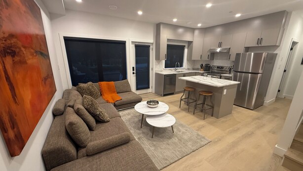 Een moderne keuken met een centraal eiland, roestvrijstalen apparatuur en een zithoek met een bank en salontafel.
