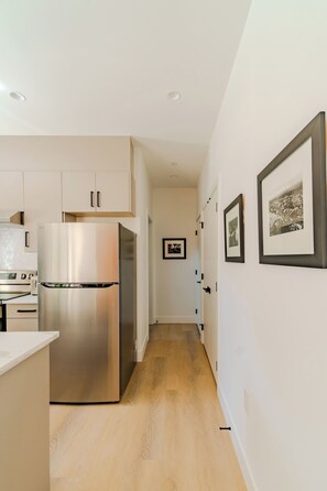 A modern kitchen with a stainless steel refrigerator, wooden flooring, and white cabinetry.