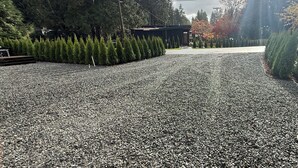 Een grindpad leidt naar een gebouw, omringd door altijdgroene bomen.