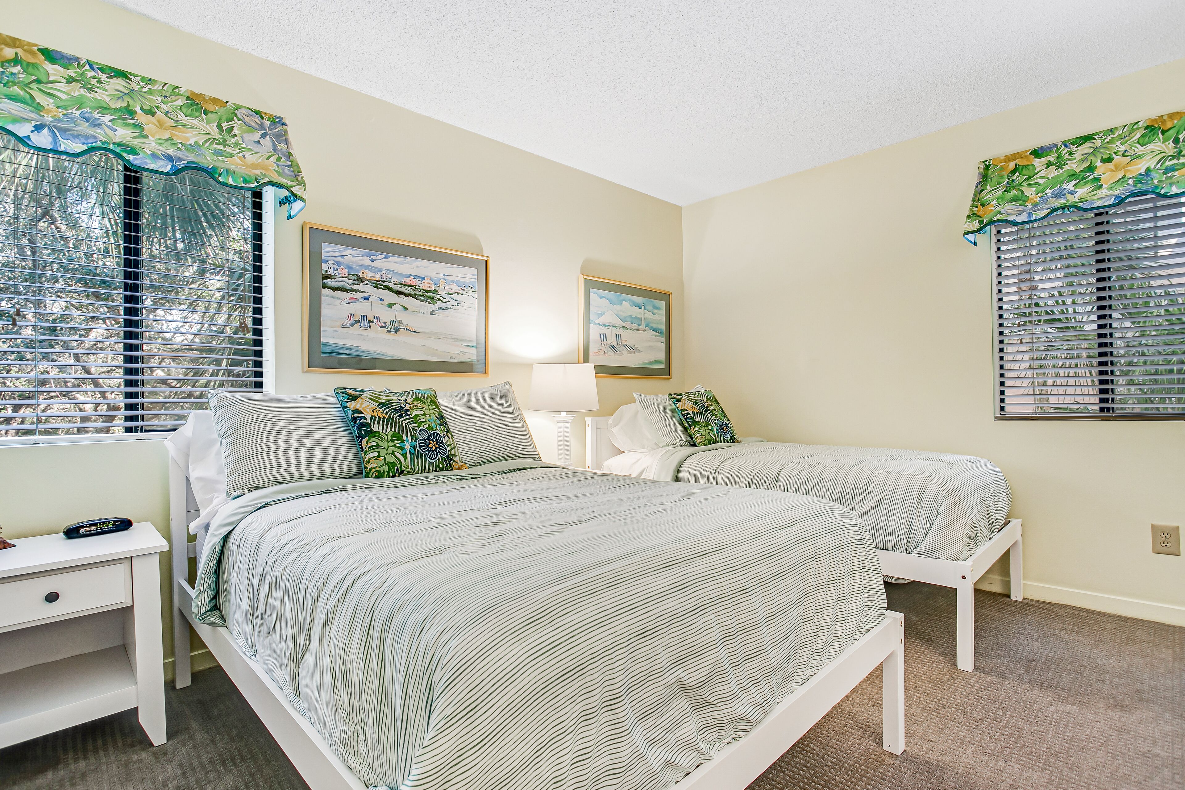A bedroom with two beds, a nightstand, and a window with blinds.