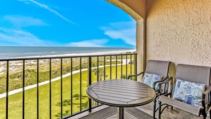 Un balcone con tavolo e due sedie, vista su una spiaggia e un campo da golf.