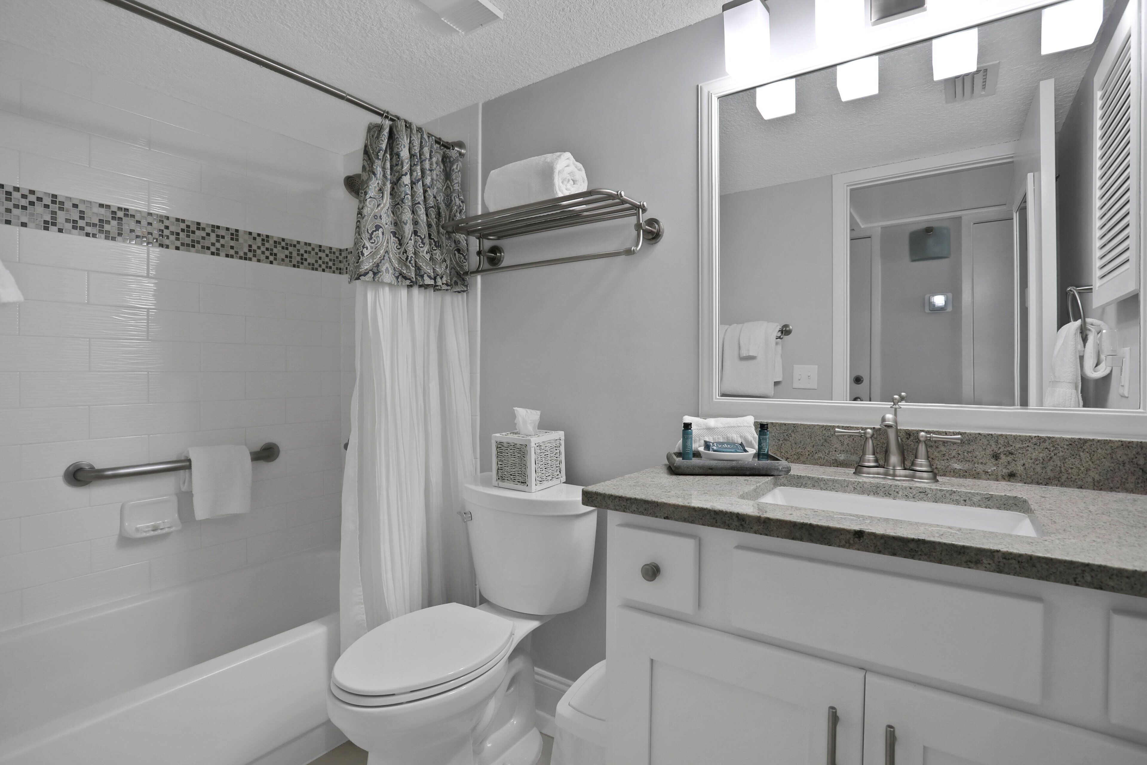 A bathroom with a toilet, shower, and sink with a mirror above.