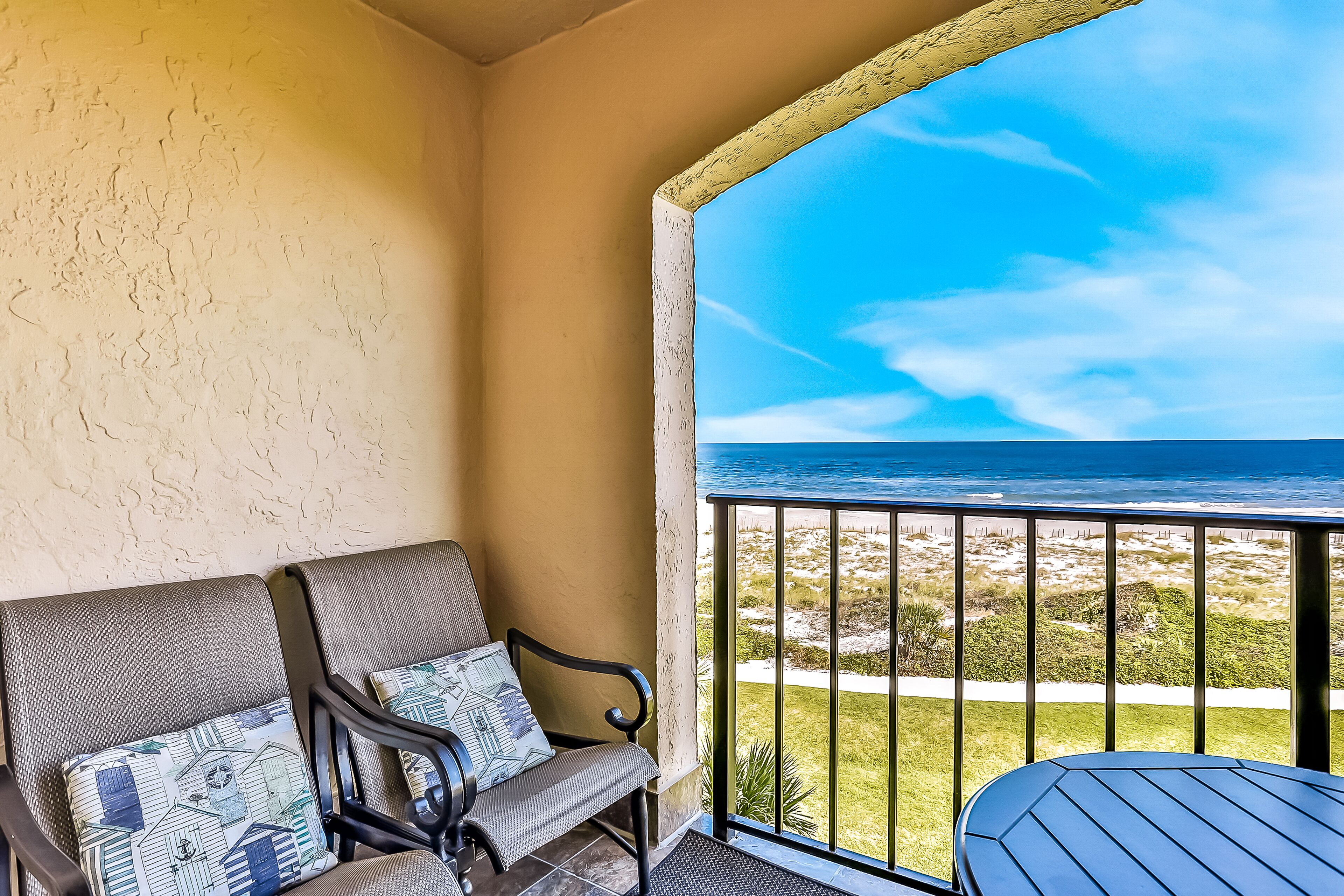 A balcony with a view of the ocean, a cushioned bench, and a small table.