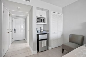 A compact hotel room with a kitchenette, a microwave, a refrigerator, and a seating area.