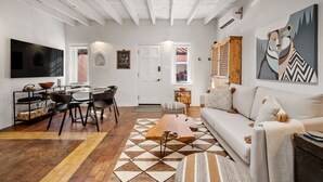 A spacious living room with a sofa, coffee table, and dining area with chairs and a table. - El Vaso Lleno - Fantastic Location, Historic Home (Santa Fe)