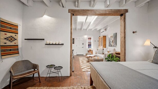 A cozy bedroom with a bed, a bench, and a small table. There is a door leading to another room. - El Vaso Lleno - Fantastic Location, Historic Home (Santa Fe)