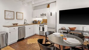 A modern kitchen with white cabinets, a dining area with a round table, and a large black screen on the wall. - El Vaso Lleno - Fantastic Location, Historic Home (Santa Fe)