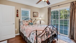 A bedroom with a bed, ceiling fan, window with blinds, and a view of the outdoors.
