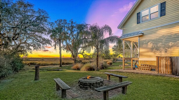 A backyard with a fire pit, picnic tables, and a house with a porch.