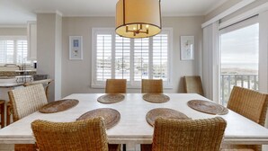 A dining area with a white table, wicker chairs, and a hanging light fixture. - Oceanfront townhome with lovely ocean view, pool, fast WiFi & W/D (Fernandina Beach)