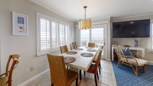 A dining area with a long table, wicker chairs, and a ceiling light. - Oceanfront townhome with lovely ocean view, pool, fast WiFi & W/D (Fernandina Beach)