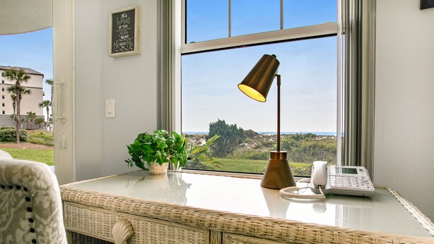 A room with a wicker desk, a potted plant, a lamp, and a phone. - Luxe, Updated, Oceanfront Condo with Ground-Floor Patio, WiFi & Shared Pool (Fernandina Beach)