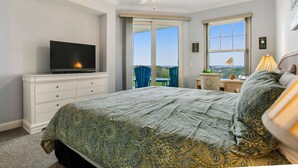 A bedroom with a bed, a television on a dresser, a ceiling fan, and a view of the outdoors through a sliding door. - Luxe, Updated, Oceanfront Condo with Ground-Floor Patio, WiFi & Shared Pool (Fernandina Beach)