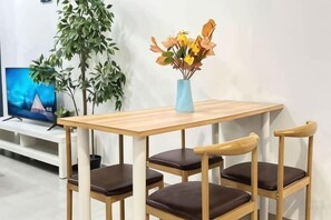 Une table en bois sur laquelle est posé un vase de fleurs, deux chaises, un téléviseur et une plante en pot.