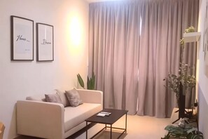 A modern living room with a sofa, a coffee table, and a large window with curtains. - JetPad Suites - Near KLIA (Dengkil)
