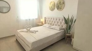A neatly made bed with white linens and heart-shaped towels, a round mirror on the wall, and a potted plant beside the bed. - JetPad Suites - Near KLIA (Dengkil)