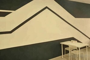 Une pi èce avec une table et une chaise blanches, un motif géométrique sur le mur et une vue partielle sur un lit.