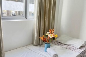 A hotel room with a bed, a window, and a vase of flowers on the nightstand. - JetPad Suites - Near KLIA (Dengkil)