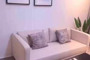 A beige sofa with two pillows, a black coffee table, and a potted plant. - JetPad Suites - Near KLIA (Dengkil)
