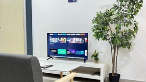 A modern office space with a flat-screen TV displaying various apps, a potted plant, and a grey chair. - JetPad Suites - Near KLIA (Dengkil)