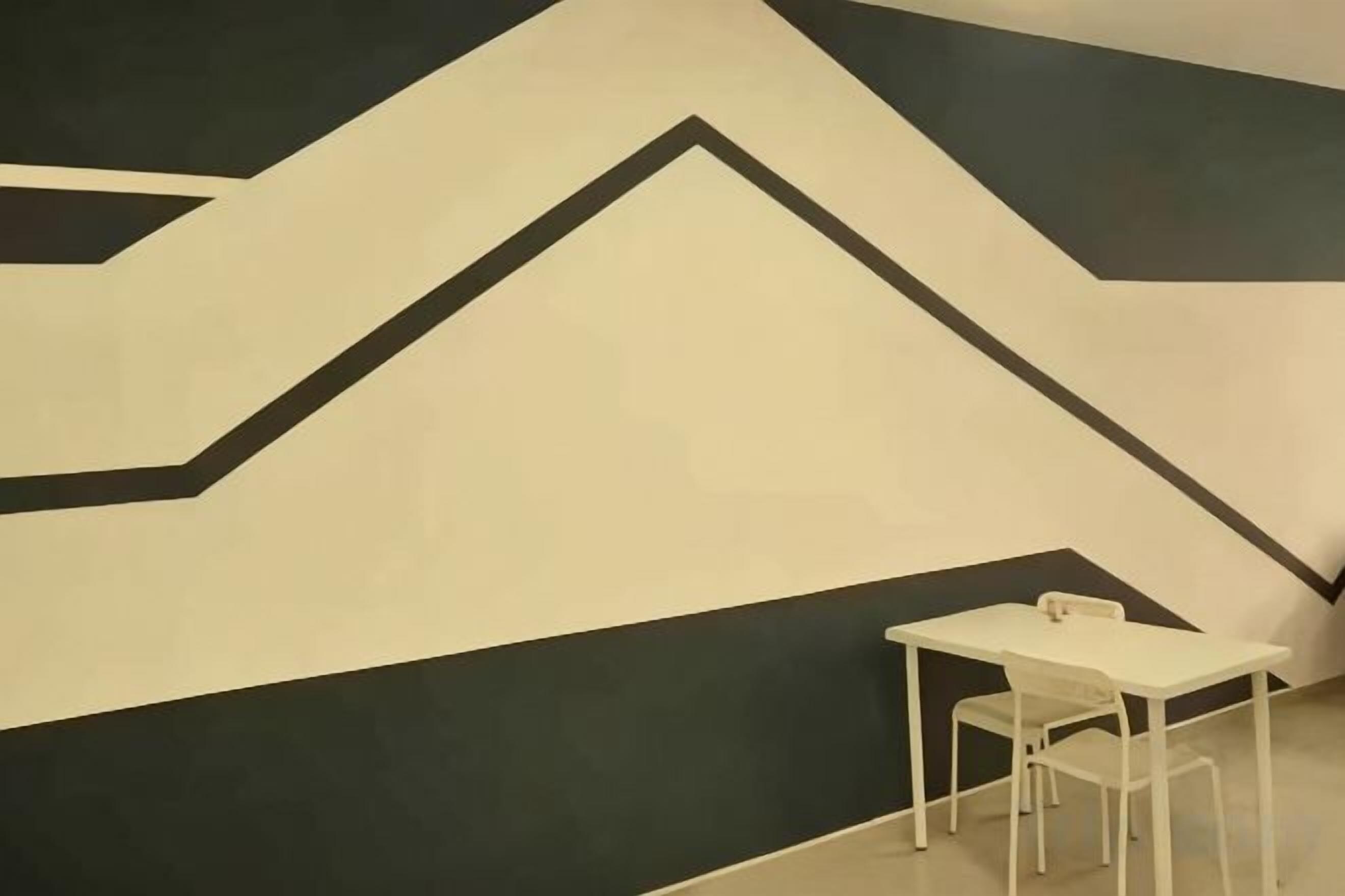 A room with a white table and chair, a geometric wall design, and a plain floor.
