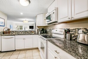 A kitchen with white cabinets, a granite countertop, a microwave, a stove, and a toaster.