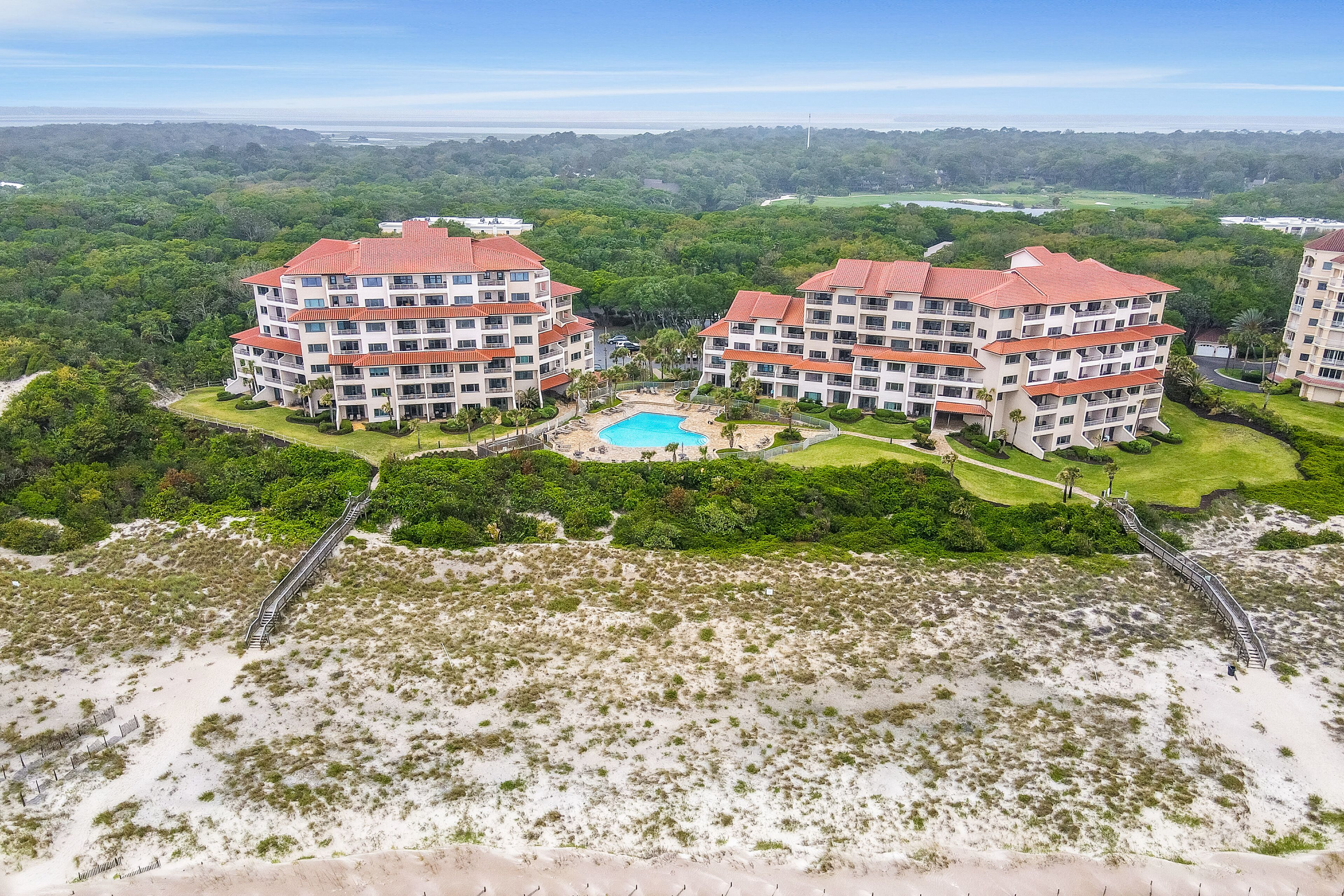 Um hotel com vários andares, piscina, cercado por vegetação exuberante e uma praia.