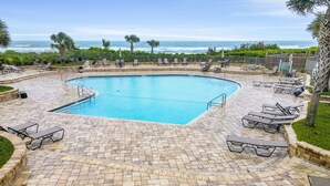 A pool area with a curved pool, lounge chairs, and a view of the ocean. - Beautiful Condo with Gorgeous Ocean Views from Balcony + Shared Pool & Free WiFi (Fernandina Beach)