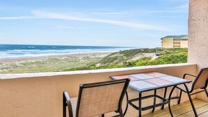 A balcony with a table and chairs overlooking a beach and ocean. - Beautiful Condo with Gorgeous Ocean Views from Balcony + Shared Pool & Free WiFi (Fernandina Beach)