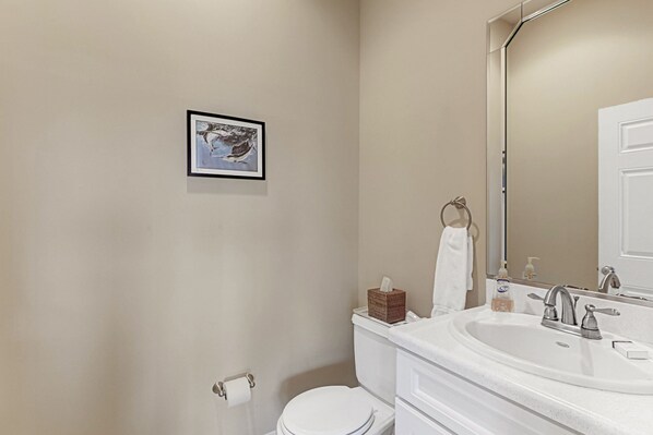 A bathroom with a toilet, sink, and a framed picture on the wall.