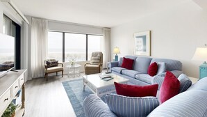 Un salon moderne avec une grande fenêtre, un ensemble de canapés, une table basse et un téléviseur.