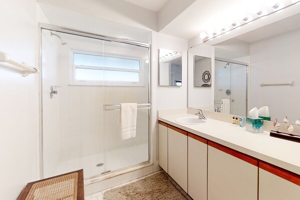 A modern bathroom with a glass shower door, a vanity with a sink, and a large mirror.