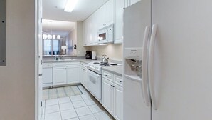 Une cuisine moderne avec des meubles blancs, un four à micro-ondes encastré, une cuisinière et un réfrigérateur.