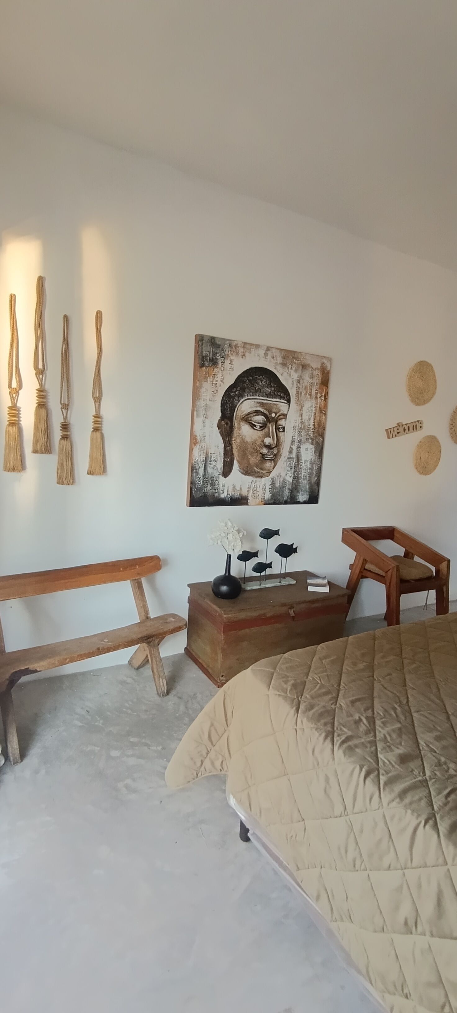 Een slaapkamer met een bed, een houten bankje, een klein tafeltje met decoratieve objecten en een aan de muur hangend schilderij.