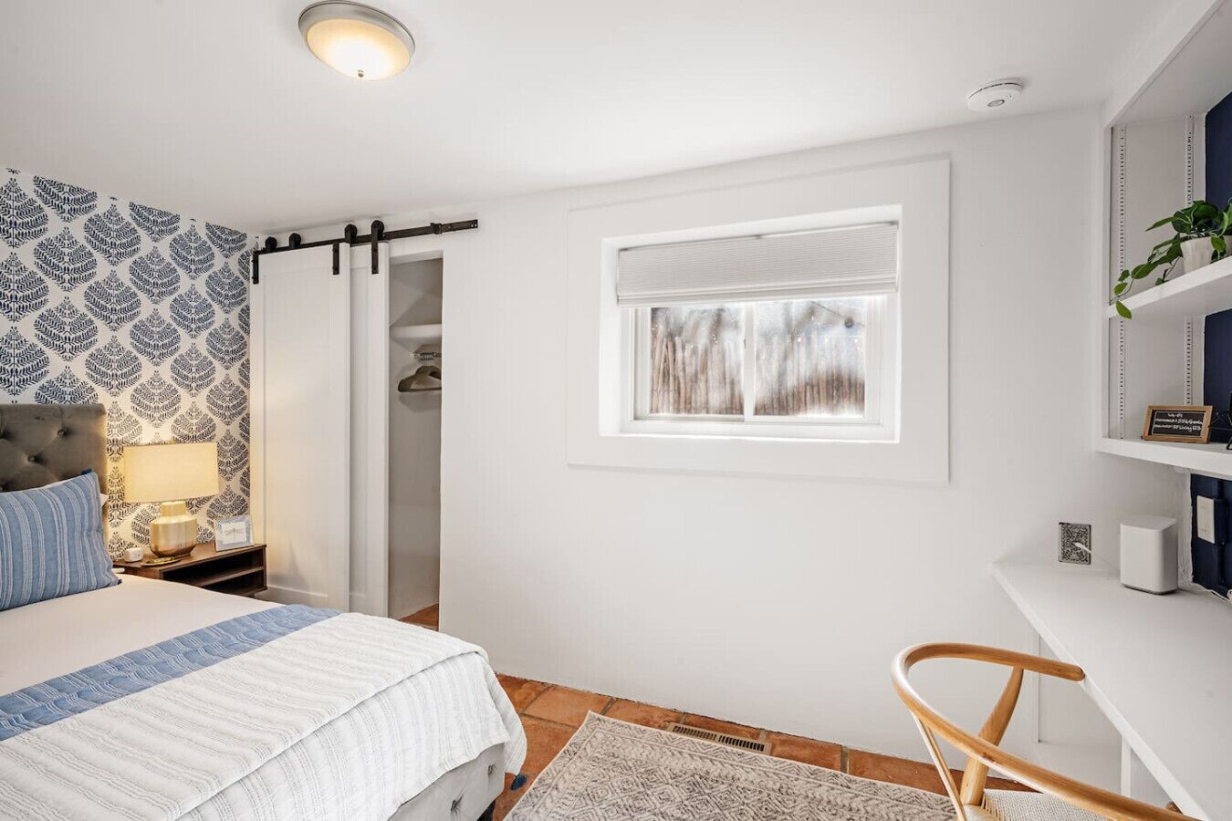 A bedroom with a bed, a nightstand, a dresser, a window with a view, and a chair.