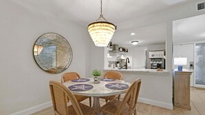 A dining area with a round table, wicker chairs, a hanging chandelier, a round mirror, and a kitchen in the background. - Dog-friendly Beachwood home in Omni Plantation with pool & beach access (Fernandina Beach)