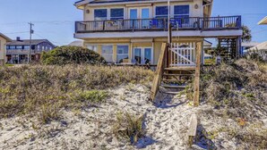 A two-story beach house with a balcony, a wooden deck, and a sandy beach in the foreground. - Spacious Beachfront Home w/Deck, Balcony, Central A/C, Washer/Dryer, and WiFi (Fernandina Beach)