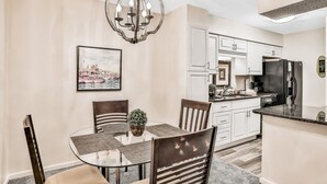 A dining area with a glass table, wooden chairs, a chandelier, and a kitchen with white cabinets and a black refrigerator. - Quiet coastal escape within walking distance to beach with shared pool (Fernandina Beach)