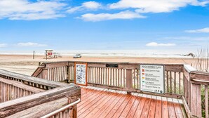 A wooden boardwalk with a beach warning sign, a lifeguard tower, and a car on the beach. - Quiet coastal escape within walking distance to beach with shared pool (Fernandina Beach)