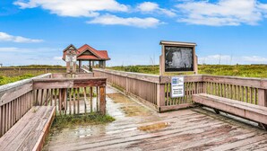 A wooden boardwalk leading to a small structure with a red roof, a signboard, and a bench. - Quiet coastal escape within walking distance to beach with shared pool (Fernandina Beach)