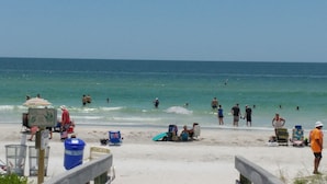A beach with people swimming and sunbathing, a lifeguard stand, and beach chairs.