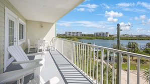 A balcony with white Adirondack chairs and a view of a river and buildings.