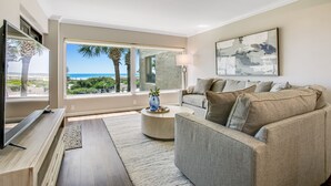 Un salon moderne doté d’une grande fenêtre, d’un téléviseur à écran plat, d’un canapé beige et d’une table basse.