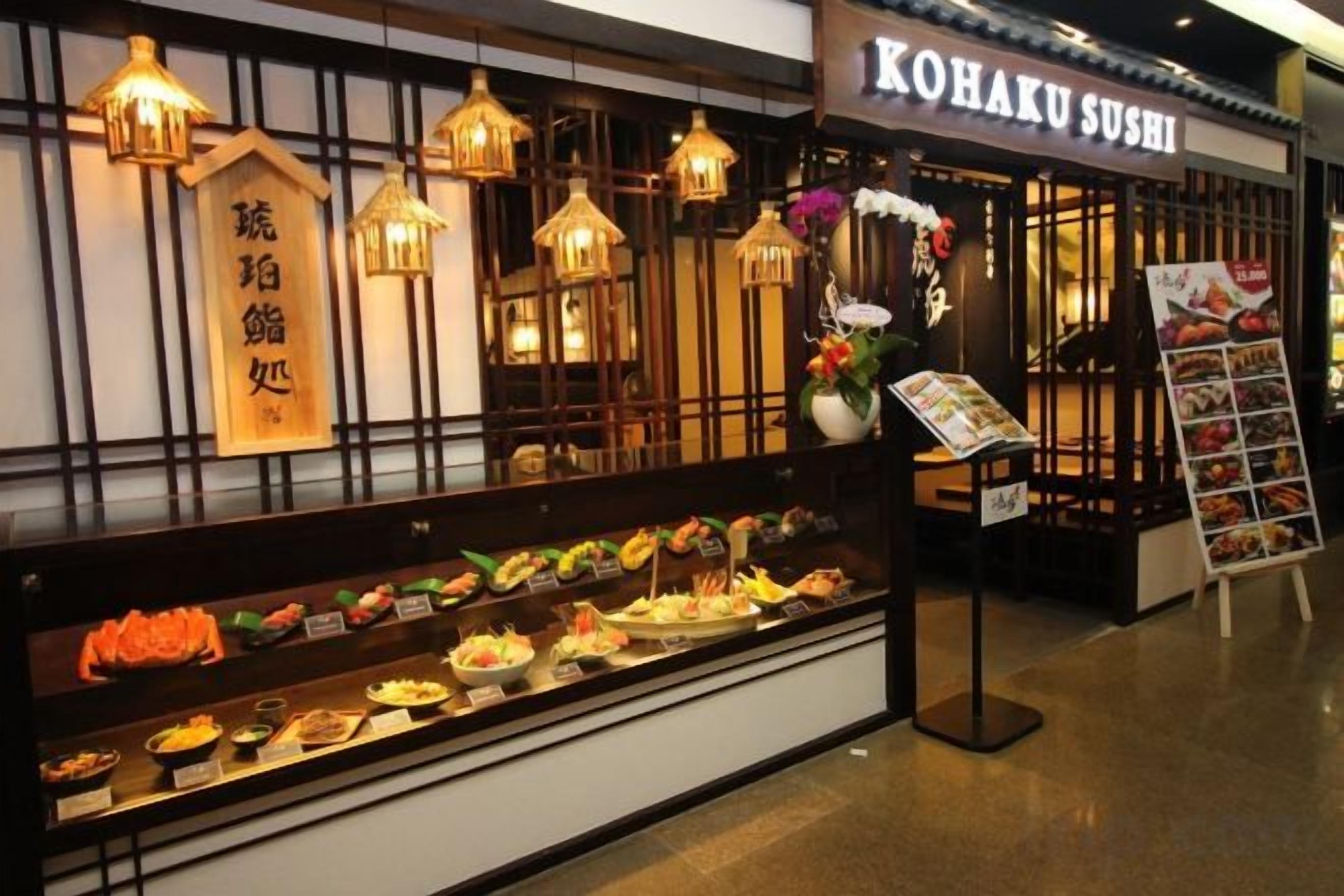 A sushi restaurant with a display case of various dishes and a menu stand outside.