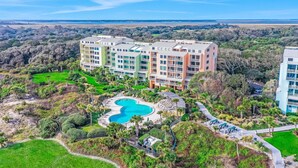A multi-story hotel with a swimming pool surrounded by greenery and a view of the landscape. - Oceanfront condo with balcony, AC, views & outdoor pool - dog-friendly (Fernandina Beach)