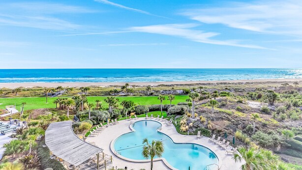 A pool with a unique shape surrounded by lounge chairs and palm trees, overlooking a beach and ocean. - Oceanfront condo with balcony, AC, views & outdoor pool - dog-friendly (Fernandina Beach)