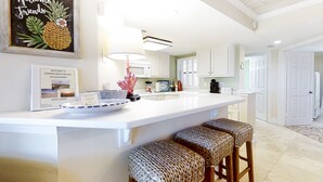 A kitchen with a white countertop, a welcome sign, a guest guide, and wicker bar stools. - Beachfront condo with outdoor pool, patio & washer/dryer - dog-friendly (Fernandina Beach)