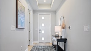 A hallway with a patterned rug, a console table with a lamp, and a door with frosted glass panels.