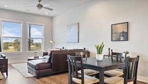 A modern living room with a brown leather sofa, a dining table with chairs, and a potted plant.